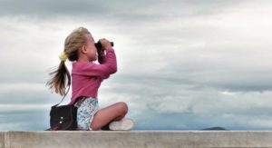 cute-young-girl-with-blonde-hair-looking-through-binoculars-taking-in-the-view-or-looking-into-the_t20_roxwVz